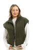 A woman with light brown hair smiles with her eyes closed, wearing the Katydid Olive Corduroy Puffer Vest over a white long-sleeve shirt, standing against a plain white background.