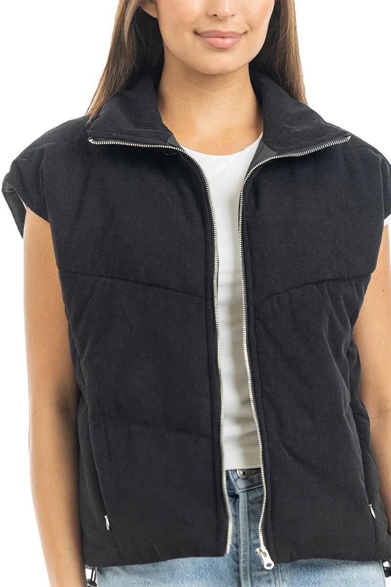 A woman stands facing forward with her hands at her sides, wearing the Katydid Black Corduroy Trendy Puffer Vest over a white t-shirt and light blue jeans.