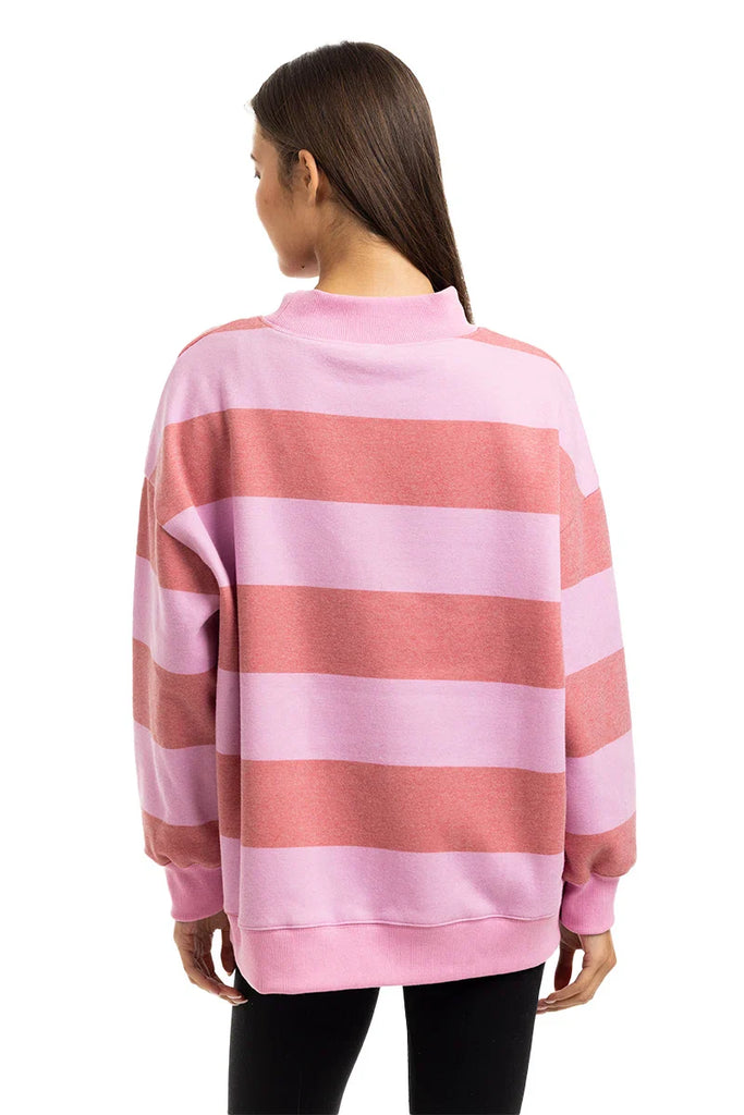 A woman with long brown hair faces away, wearing the Katydid Pink and Light Pink Striped Mockneck Pullover and black leggings against a plain white background.
