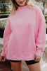 A woman smiles outdoors, wearing the Katydid Pink Essential Mockneck Crew and black shorts, with her hands relaxed by her sides. Only her upper body and part of her legs are visible.