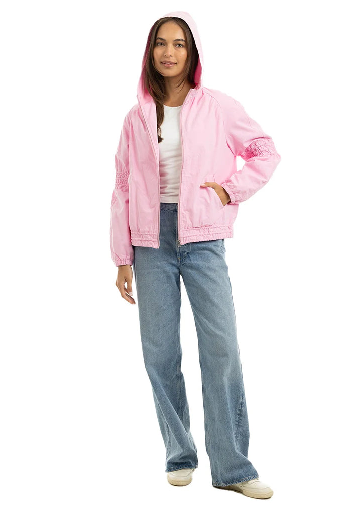 A woman models the Katydid Pink Lightweight Casual Hooded Jacket over a white t-shirt, blue wide-leg jeans, and white sneakers against a white background.
