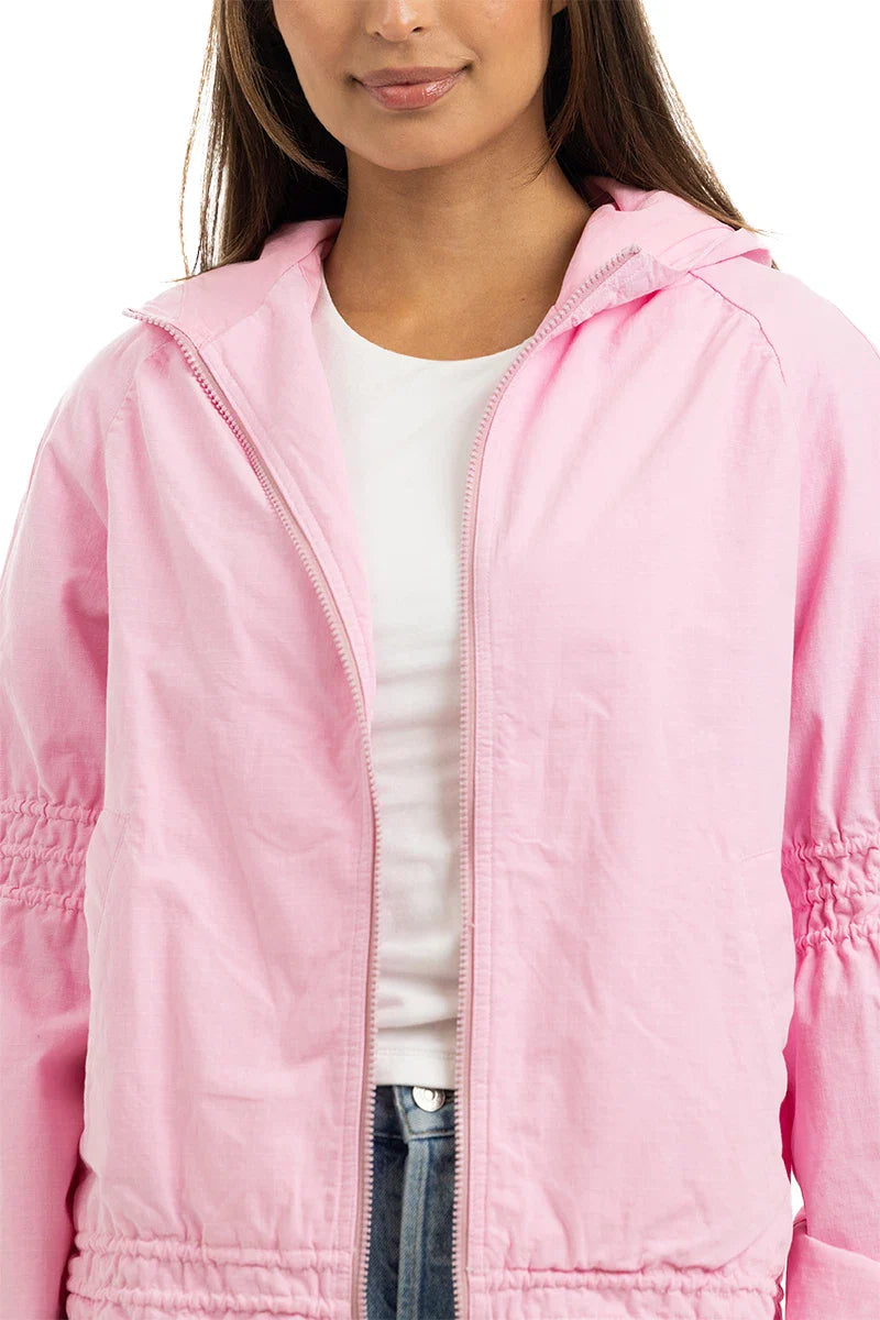 A person wears the Katydid Pink Lightweight Casual Hooded Jacket over a white t-shirt, with only the lower face and upper torso visible. This women’s jacket features a hood, gathered sleeves, and adds a stylish, lightweight layer.