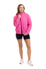 A woman poses against a white background in the Katydid Hot Pink Sporty Diamond Quilted Jacket, paired with black shorts and white sneakers. She holds the jackets collar with one hand and looks to the side, smiling slightly.