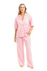A person stands barefoot in the Love Joy  Peace Preppy PJ Set by Katydid, featuring pink womens pajama pants and a matching button-up top with small orange animal prints, against a white background.