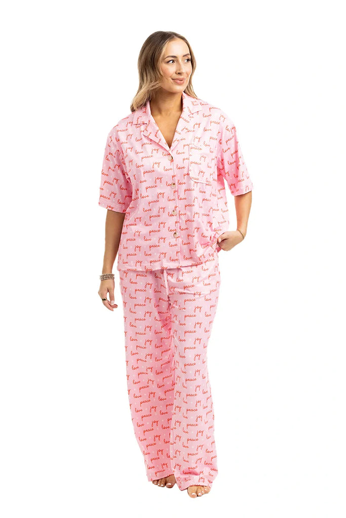 A woman smiles and looks to the side wearing the Katydid Love Joy  Peace Preppy PJ Set—pink animal print pajama pants with a matching button-up top—perfect cozy Christmas pajamas, pictured against a white background.