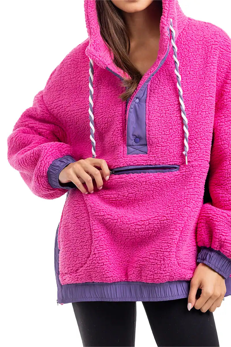 A woman wears the Katydid Hot Pink Two-Toned Sherpa Pullover Jacket, featuring a purple kangaroo pocket, purple trim, and white drawstrings. The cozy, textured pullover is shown from her shoulders to thighs.
