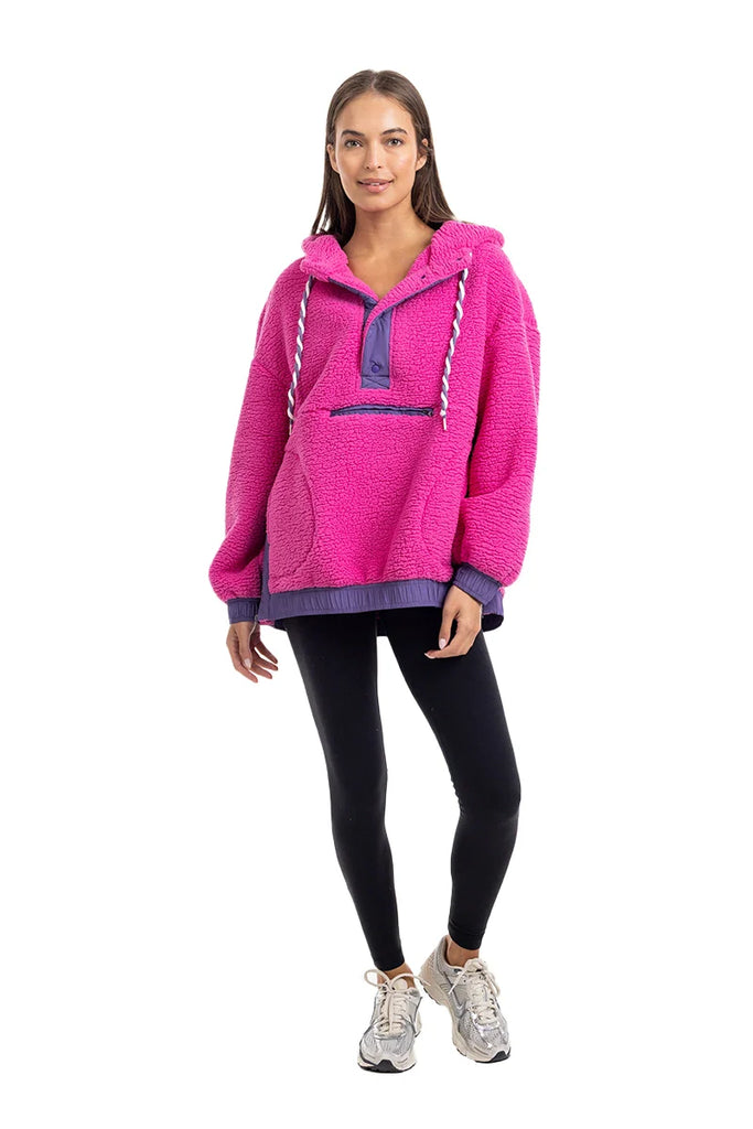 A woman faces forward in a Katydid Hot Pink Two-Toned Sherpa Pullover Jacket with white drawstrings, paired with black leggings and white sneakers. The cozy pullover stands out against the plain white background.