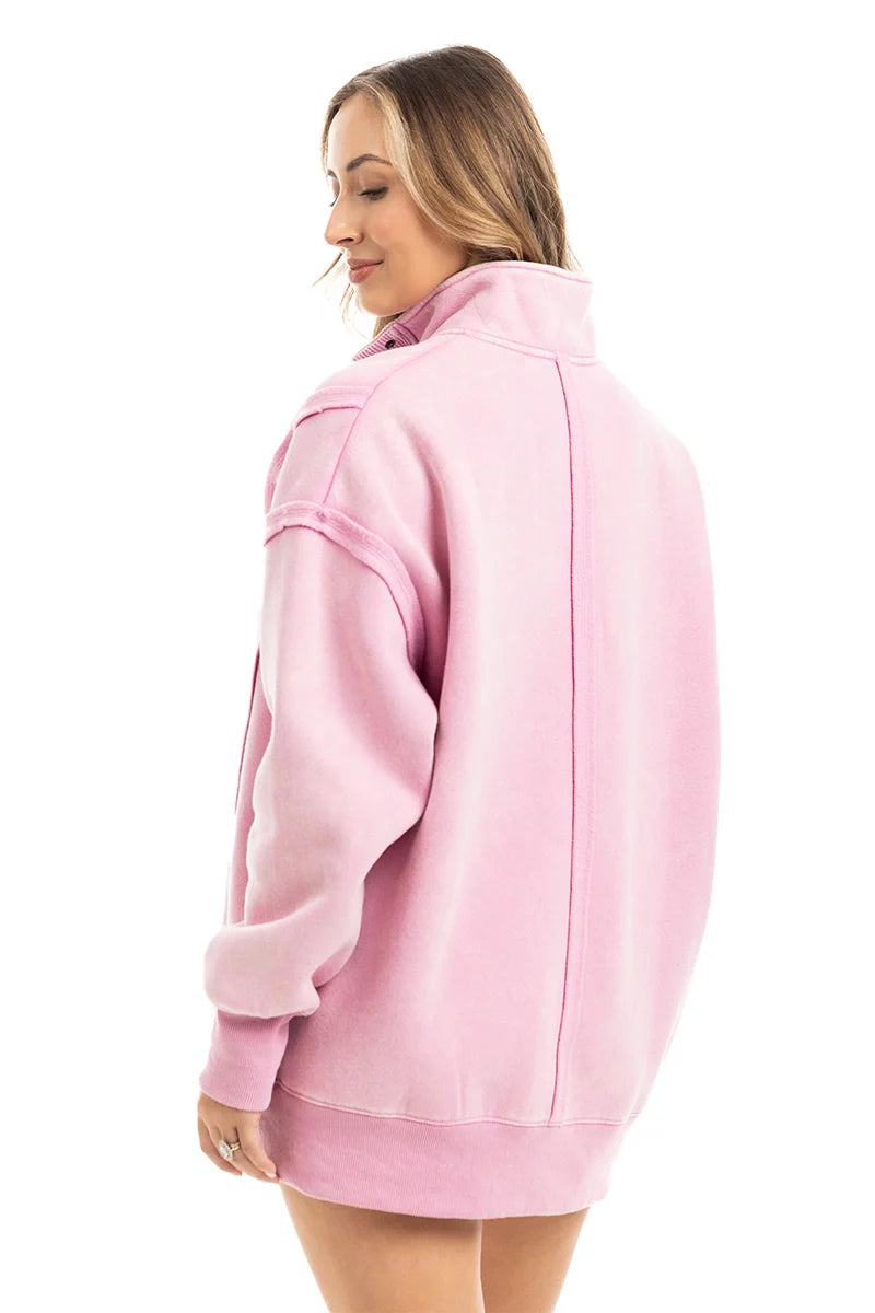 A woman with light brown hair faces away, wearing the Katydid Pink Vintage Wash Pullover for Ladies featuring dropped shoulders and a high collar. She stands against a plain white background.