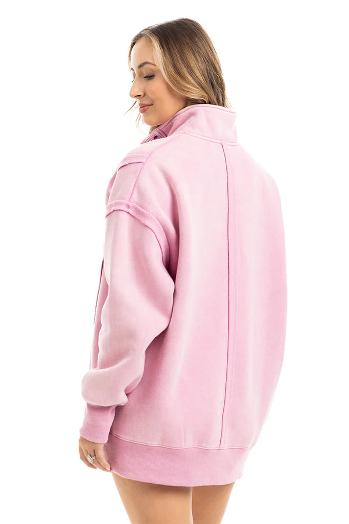 A woman with light brown hair faces away, wearing the Katydid Pink Vintage Wash Pullover for Ladies featuring dropped shoulders and a high collar. She stands against a plain white background.