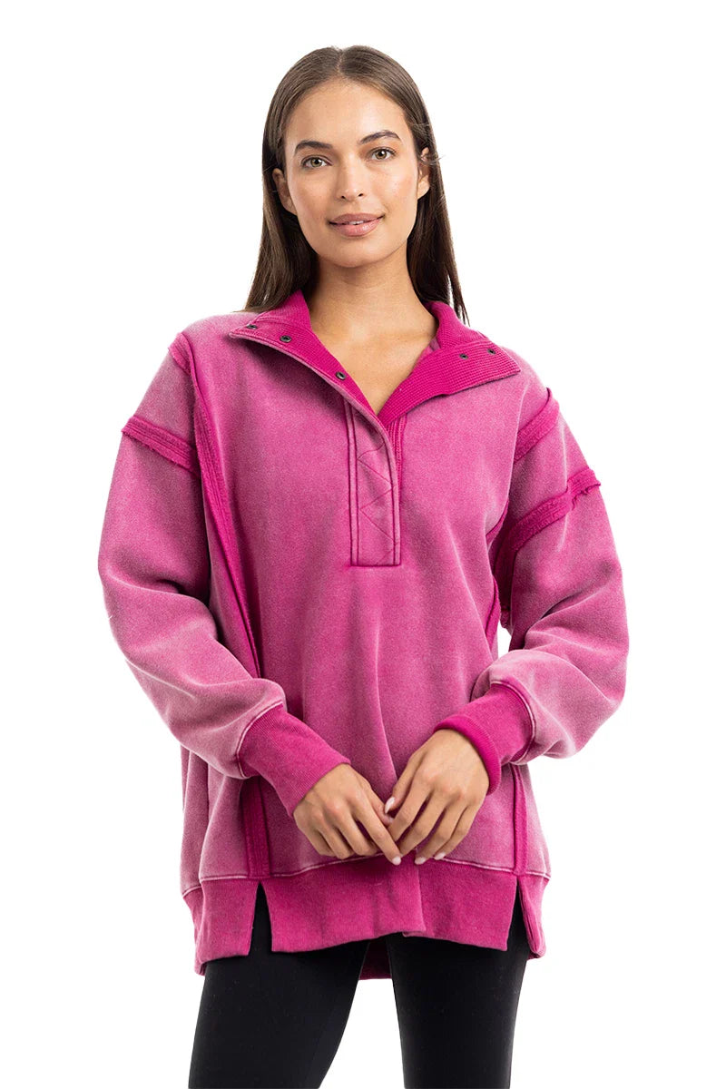 A woman with straight brown hair wears the Katydid Hot Pink Vintage Wash Pullover Womens, featuring snap buttons at the collar and side slits, paired with black leggings, standing against a white background.