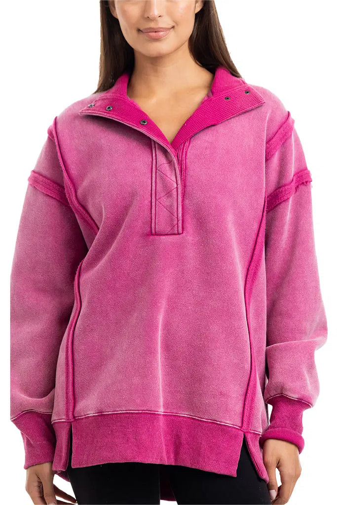A woman wears the Katydid Hot Pink Vintage Wash Pullover, a loose-fitting womens sweatshirt with long sleeves, a snap-neck collar, and exposed stitching.