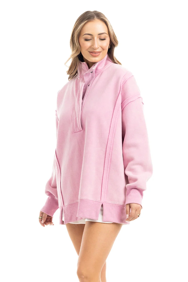 A woman models the Katydid Pink Vintage Wash Pullover for Ladies—an oversized, light pink top with long sleeves and side slits—standing against a white background and smiling gently with her eyes closed.