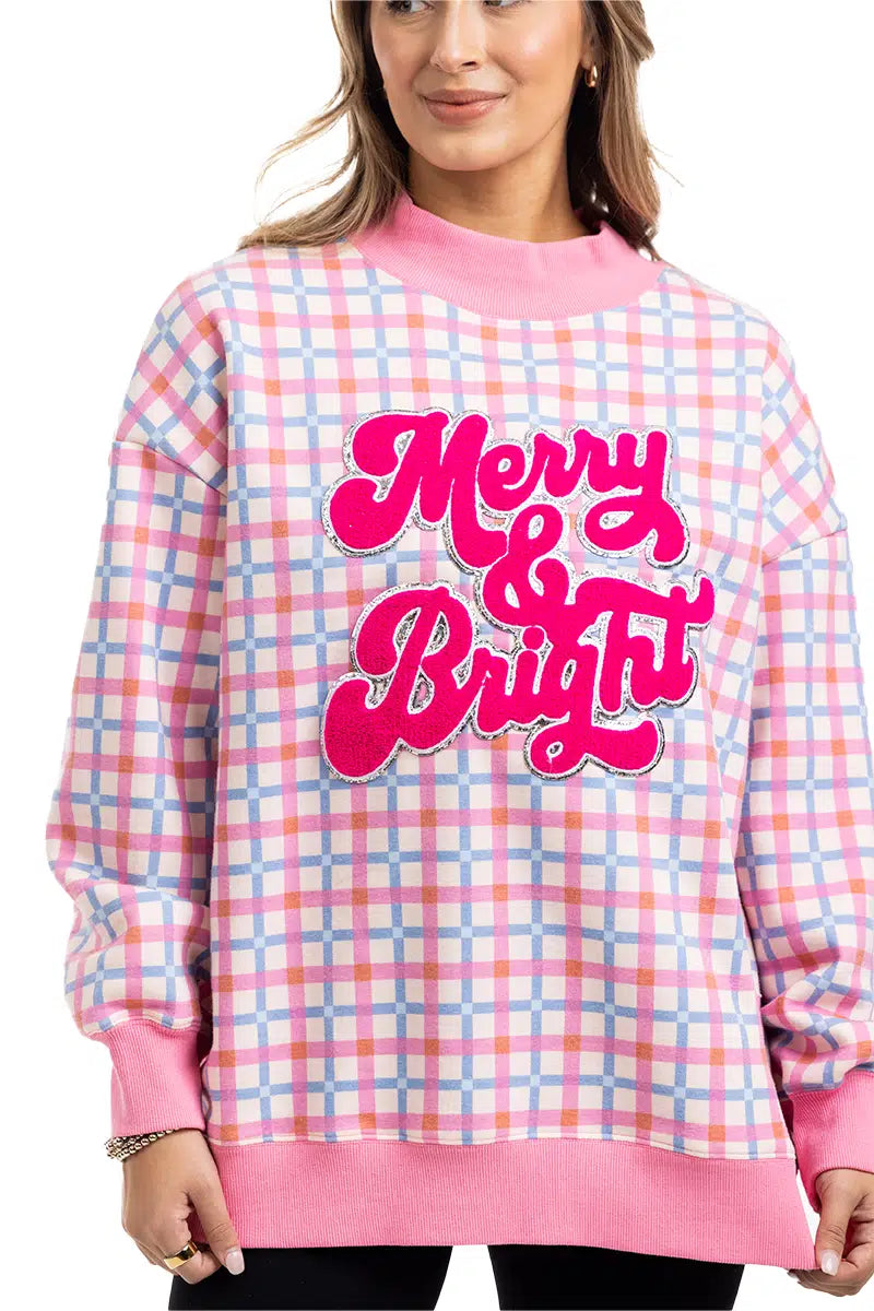 A woman with light brown hair smiles slightly, wearing the Katydid Merry  Bright Plaid Mockneck Sweatshirt for women, featuring pink, blue, and white plaid and bold pink letters on the front—a festive holiday pullover.