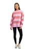 A woman with long brown hair stands facing forward against a white background, wearing the Katydid Pink and Light Pink Striped Mockneck Pullover, black leggings, and white sneakers, smiling gently with her arms relaxed at her sides.