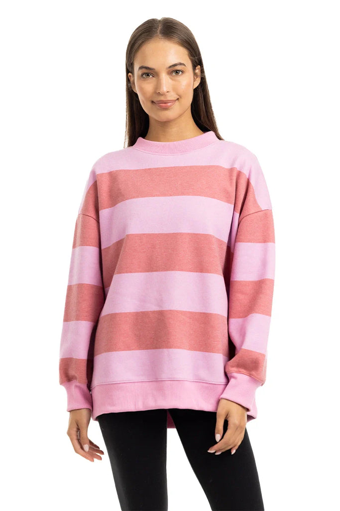 A woman with straight brown hair wears the Katydid Pink and Light Pink Striped Mockneck Pullover and black leggings, standing and smiling at the camera against a white background.