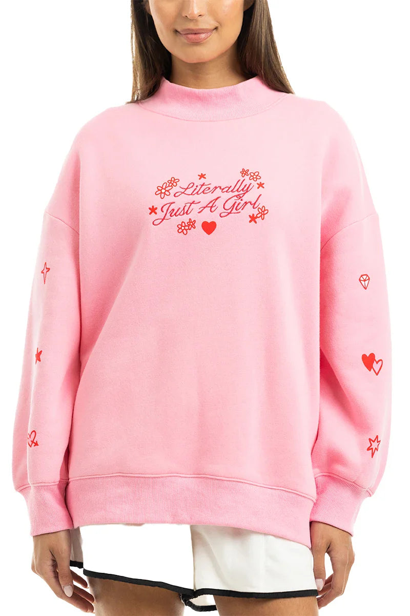 A woman wears the Katydid Literally Just A Girl Mockneck Pullover, a cute light pink sweatshirt with red text and small embroidered flower, heart, and diamond details, paired stylishly with a white skirt.