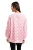 A woman with straight brown hair, seen from behind, wears a loose-fitting Katydid Joy Knit Mockneck Sweatshirt Women in pink with red script reading peace, love, and joy all over. She pairs this festive pullover with black leggings.
