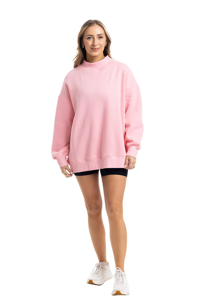 Someone stands facing forward in the Katydid Pink Essential Mockneck Crew, paired with black shorts and white sneakers, set against a plain white background.