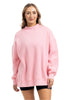 A woman faces forward, smiling, wearing the Katydid Pink Essential Mockneck Crew with black shorts against a plain white background.