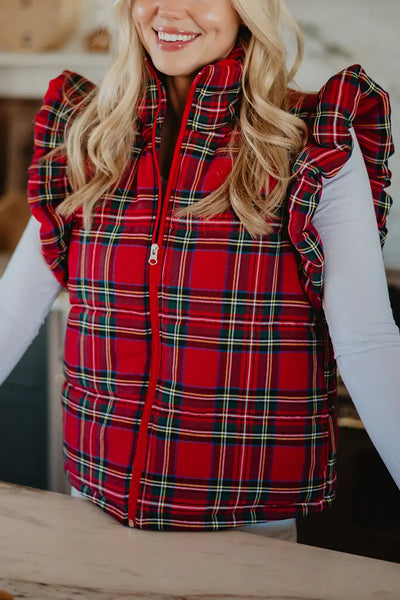 A woman smiles in a Katydid Royal Stewart Plaid Ruffle Puffer Vest over a white long-sleeve shirt. The image highlights the festive vest’s ruffled shoulders, making it an ideal choice for a cheerful holiday look.
