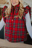 A woman smiles in a Katydid Royal Stewart Plaid Ruffle Puffer Vest over a white long-sleeve shirt. The image highlights the festive vest’s ruffled shoulders, making it an ideal choice for a cheerful holiday look.