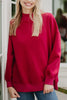 A woman with long blonde hair, smiling near a white door, wears the Katydid Red Essential Solid Mockneck with blue jeans. The softly blurred background enhances the cozy fall wardrobe vibe.
