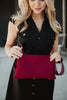A woman in a black button-down dress holds the Katydid Wine Woven Everywhere Crossbody in front of her, with focus on the bag and her hands while her face is partially out of frame—a stylish fall accessory.