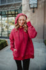 A woman enjoys a cozy, relaxed moment outdoors in the Katydid Red Heart Quilted Garment Washed Hoodie for Women, hood up and one hand in her pocket, smiling with her eyes closed and wearing black pants.