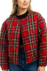 A person with light brown hair, smiling slightly, wears the Katydid Royal Stewart Plaid Holiday Quilted Jacket over a black top and blue jeans. Shown from shoulders to waist.