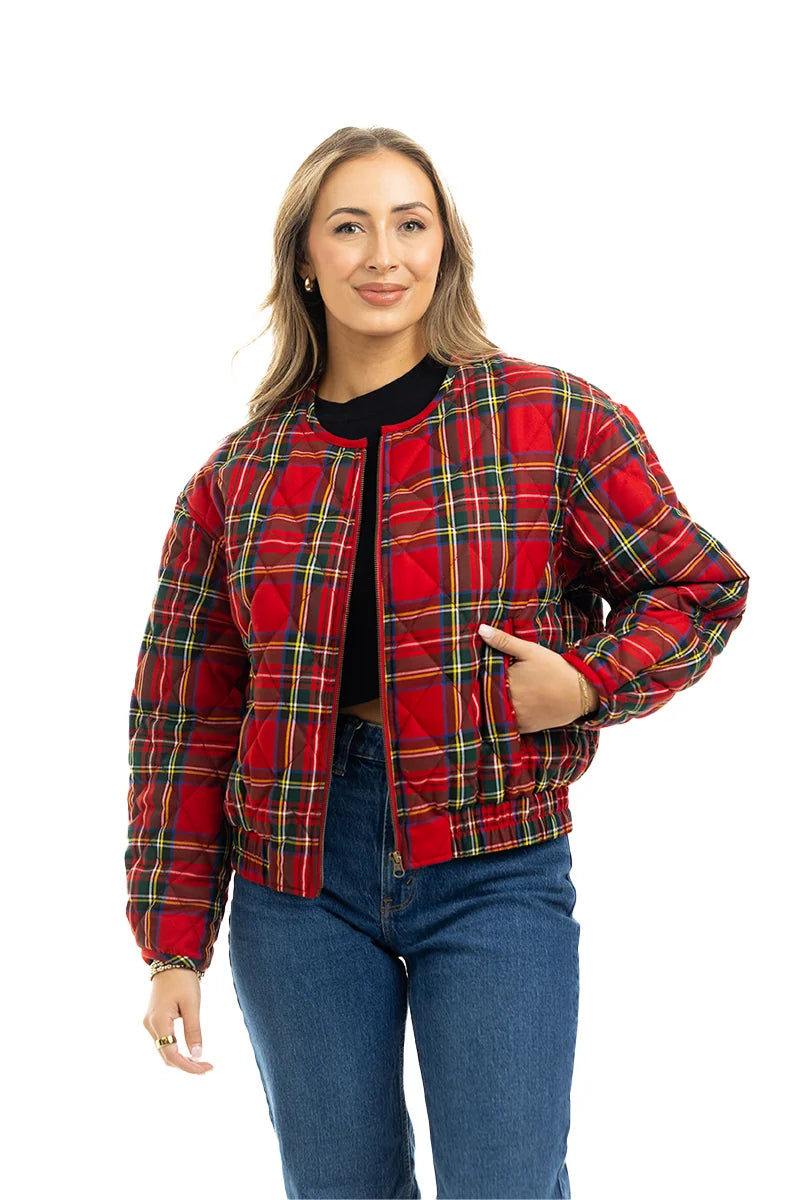 A person with long, light brown hair wears the Katydid Royal Stewart Plaid Holiday Quilted Jacket over a black top and blue jeans, standing with one hand in their pocket against a white background.
