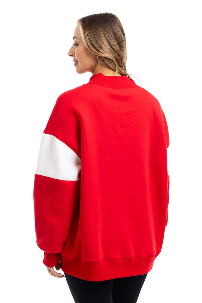 A woman with long, light brown hair wears the Katydid MERRY Womens Mockneck Top in bright red with a white sleeve stripe, standing against a white background and looking slightly to the side.