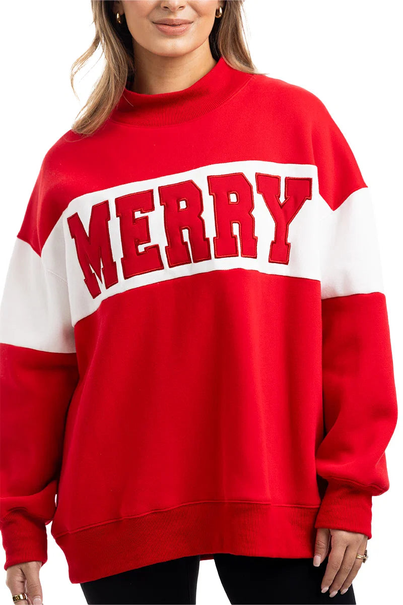A woman with long hair smiles in the Katydid MERRY Womens Mockneck Top, a red and white sweatshirt featuring MERRY in large red letters across the front, her hands relaxed at her sides.
