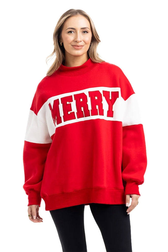 A woman smiles in a Katydid MERRY Womens Mockneck Top, featuring bold MERRY lettering, standing with her hands at her sides against a plain white background.