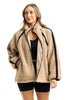 A woman models the Katydid Tan Sherpa Lace Trim Jacket over a black crop top and shorts, standing with one hand in her pocket against a white background to showcase this cozy fall piece.