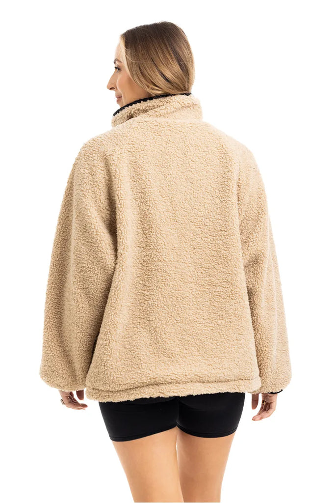 A person faces away, wearing the Katydid Tan Sherpa Lace Trim Jacket with long sleeves and black shorts, set against a white background.