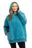 A woman smiles, wearing the Katydid Deep Teal Heart Quilted Garment Washed Hoodie with thumbholes, paired with black pants for a casual-chic style.