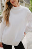 A woman with long blonde hair wears the Katydid Cloud White Essential Mockneck Sweatshirt and black pants, standing outdoors with one hand in her pocket.