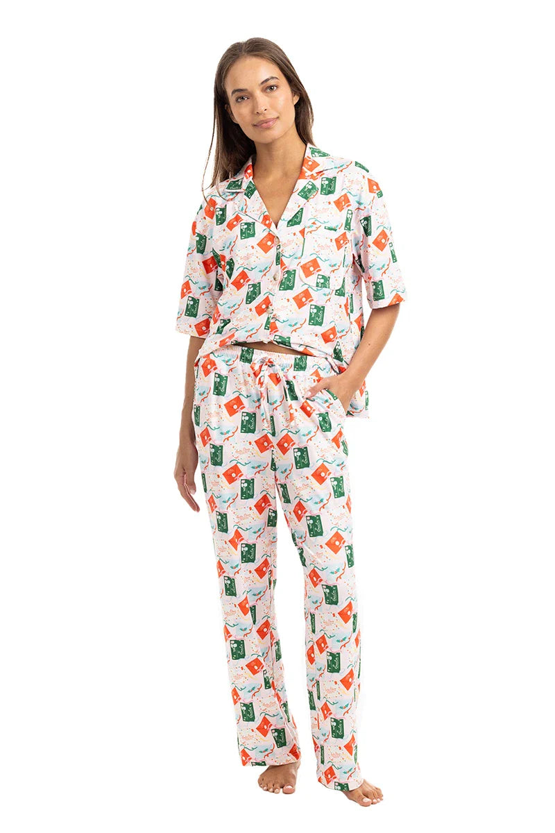 A woman wears Katydid’s Santas Mail Christmas Pajamas for Women, standing barefoot with red and green gift boxes—festive holiday sleepwear perfect for the season.
