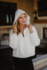 A woman with long blonde hair wears the Katydid Cloud White Lightweight Hooded Jacket with black leggings, standing indoors holding the hood and smiling slightly.