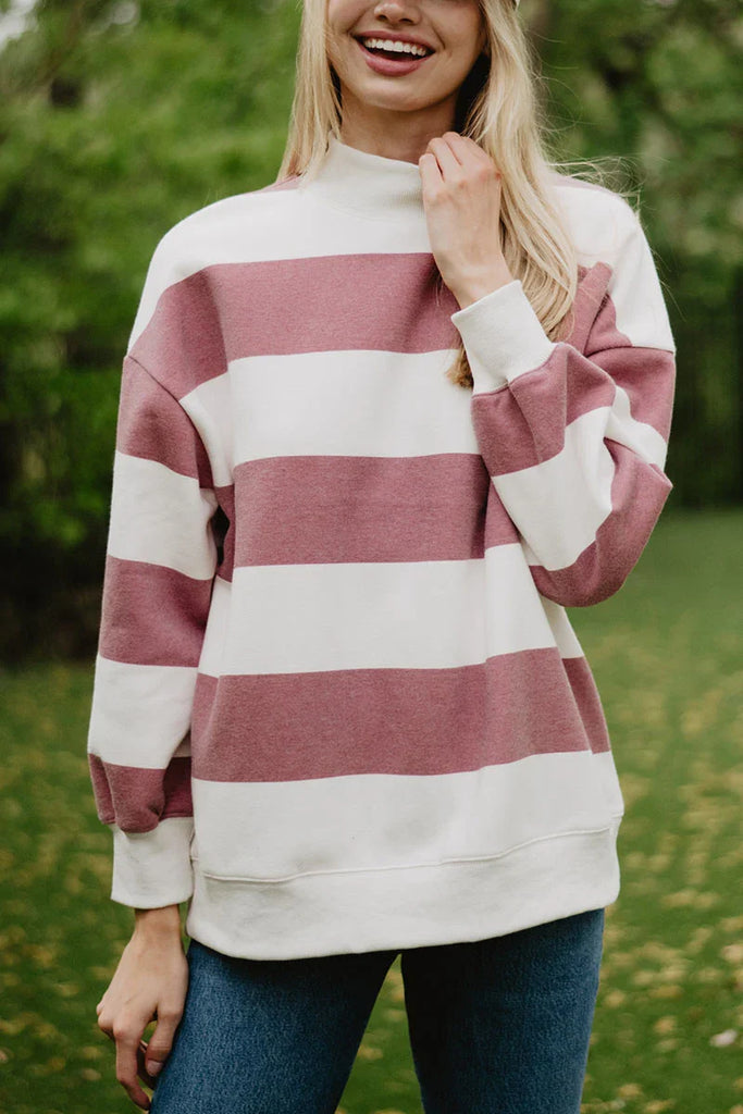 A woman outdoors smiles in the Katydid Wine and White Striped Mockneck Sweatshirt for women, paired with blue jeans. The oversized top adds gameday flair against the blurred green background.
