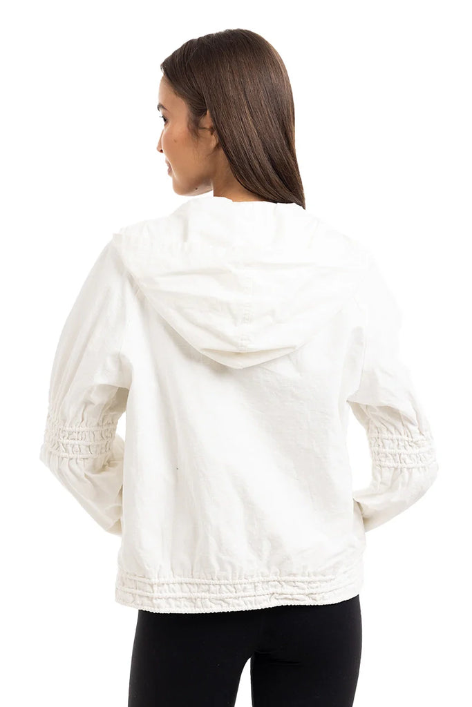 A woman with straight brown hair is seen from the back wearing the Katydid Cloud White Lightweight Hooded Jacket, featuring cinched sleeves and hem, paired with black pants against a plain white background.