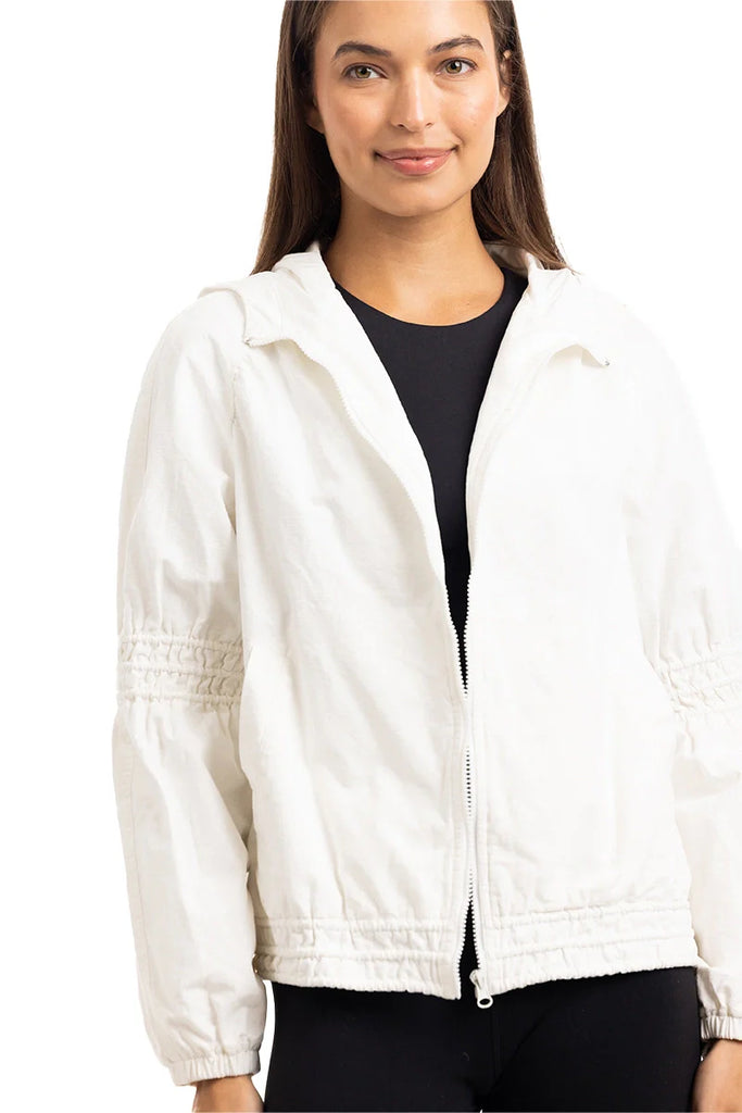 A woman smiles slightly while wearing the Katydid Cloud White Lightweight Hooded Jacket over a black top, standing against a white background.