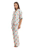 A woman stands barefoot wearing the Katydid Whimsical Bow Pajamas Set, a festive womens collared button-up shirt with matching pants in white featuring colorful bows—a perfect holiday pajama look. She poses against a white backdrop.