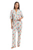 A woman stands barefoot in Katydid’s Whimsical Bow Pajamas Set, featuring a colorful abstract print with a short-sleeve button-up top and long pants—perfect festive holiday loungewear—on a white background.