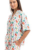 A woman wears the Katydid Whimsical Bow Pajamas Set, a colorful short-sleeved set with a playful bow print, standing with one hand in her pocket and smiling—perfect for festive holiday lounging.