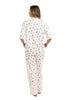 A woman stands barefoot facing away, wearing the Katydid Apres Ski Matching Pajama Pants Set with a colorful holiday print, featuring a short-sleeve top and loose-fitting long pants against a plain white background.