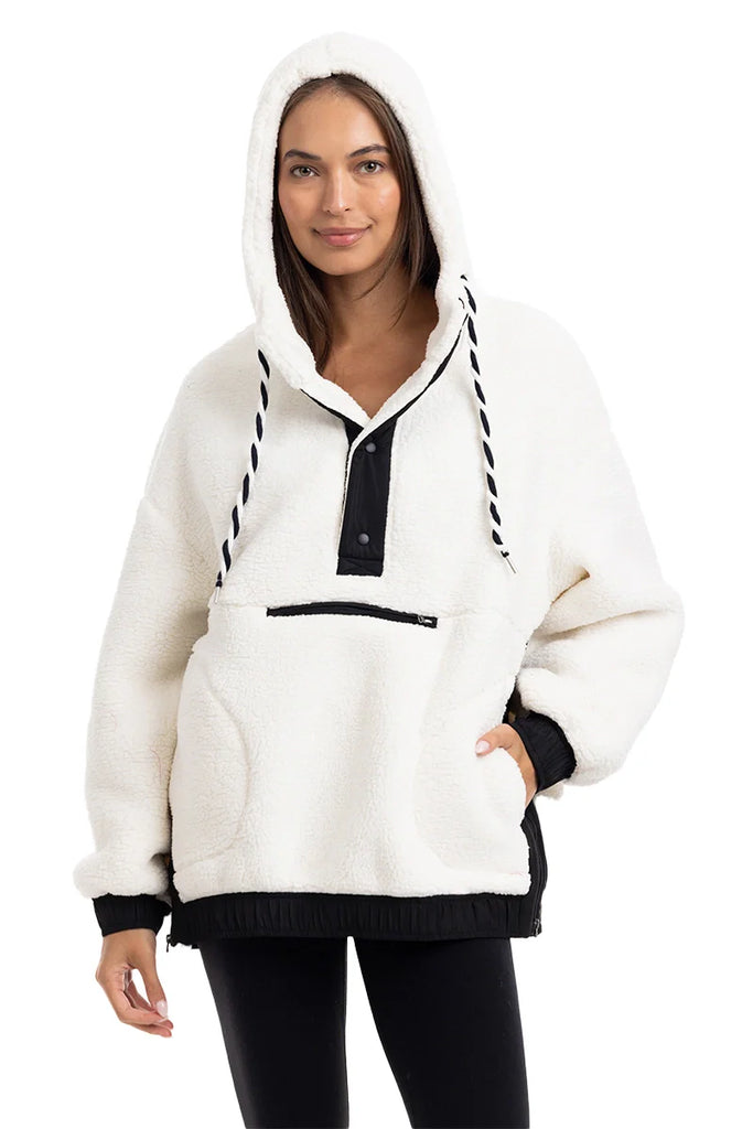 A woman models the Katydid White Womens Two-Toned Pullover Hoodie, featuring black accents, a front zipper pocket, hood with black drawstrings, and black-trimmed cuffs and hem, standing against a plain background.