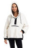 A woman models the Katydid White Womens Two-Toned Pullover Hoodie, featuring black accents, a front zipper pocket, hood with black drawstrings, and black-trimmed cuffs and hem, standing against a plain background.