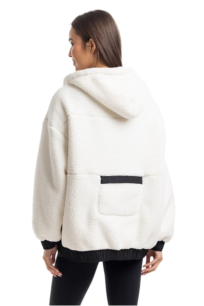 A woman with straight brown hair wears black leggings and the Katydid White Womens Two-Toned Pullover Hoodie, featuring a cozy sherpa fleece design with a black stripe and pocket detail on the lower back.