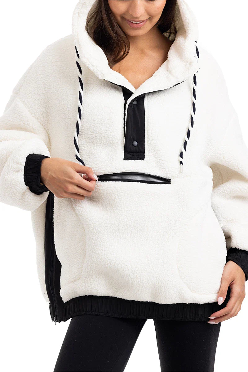 A woman in the Katydid White Womens Two-Toned Pullover Hoodie with black accents and drawstrings opens a zippered front pocket and pairs it with black leggings.